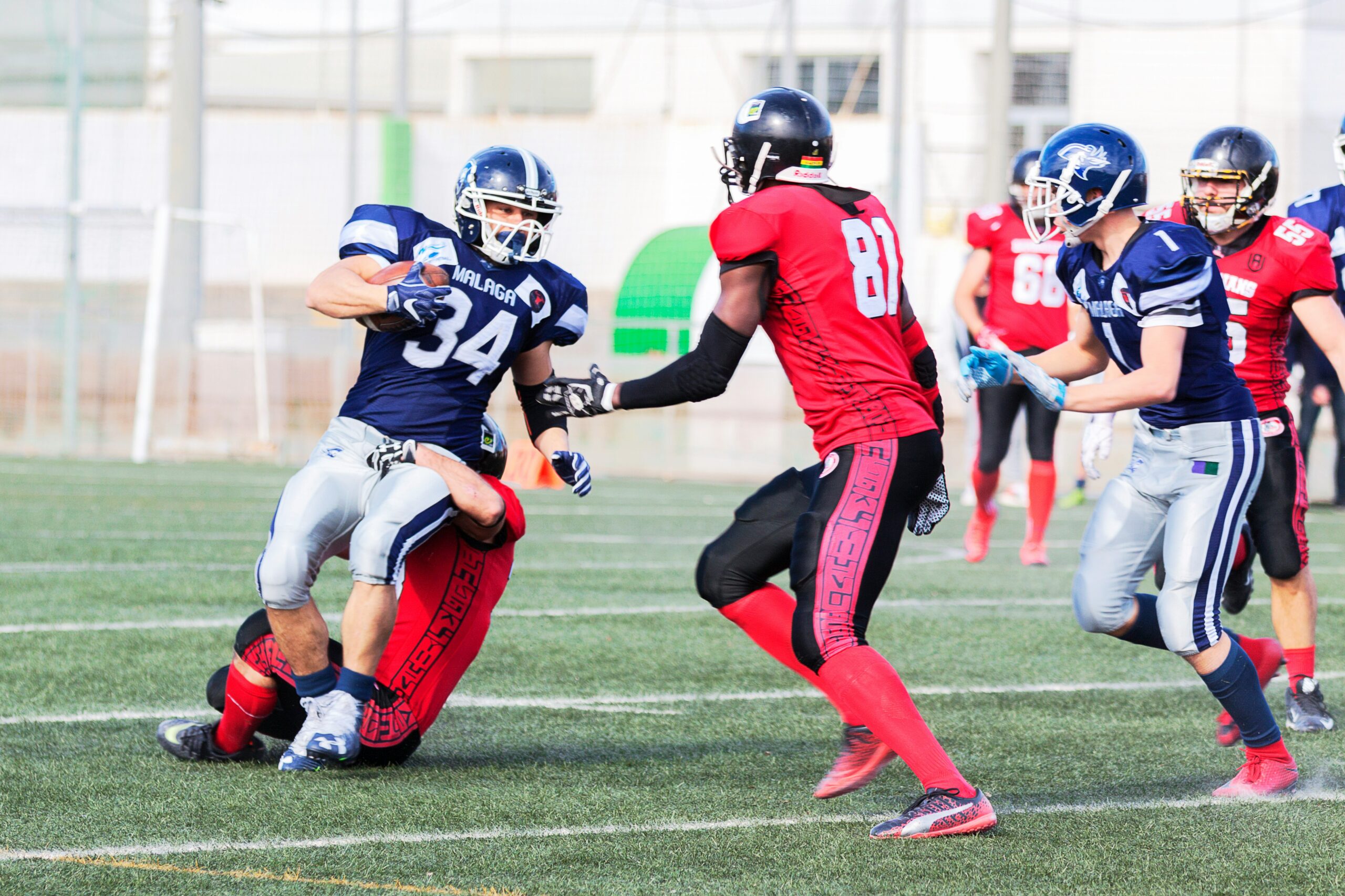 football players in red jersey shirt and red pants running on green grass field during daytime